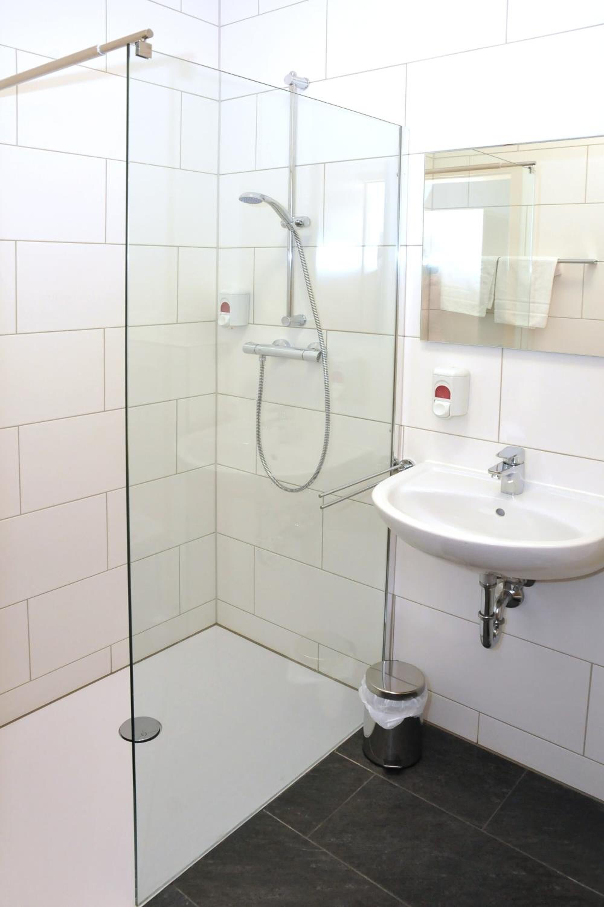 Ein modernes Badezimmer mit einer Duschkabine, einem weißen Waschbecken und einem Spiegel darüber.