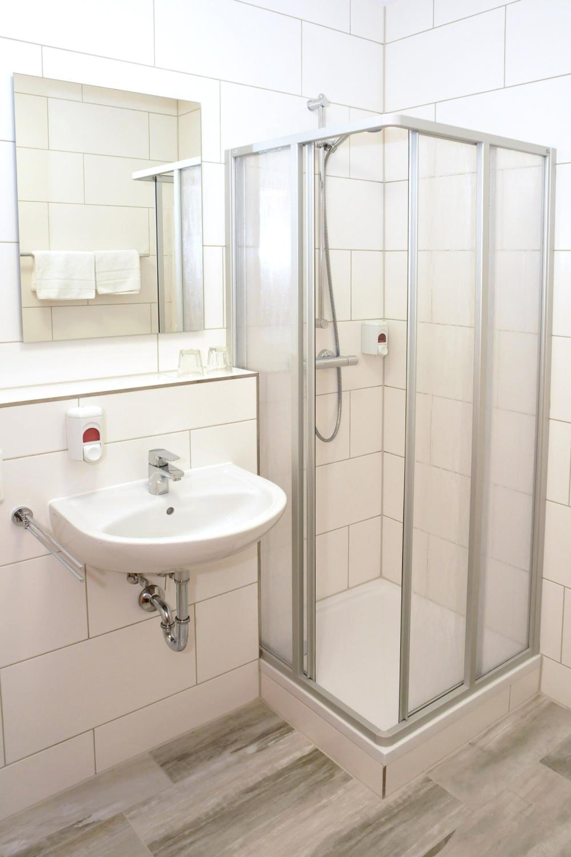 A modern bathroom with a glass-enclosed shower, a white sink, and a mirror above it.