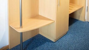 A wooden wardrobe with a hanging rod, a shelf, and a drawer, with a blue carpeted floor.