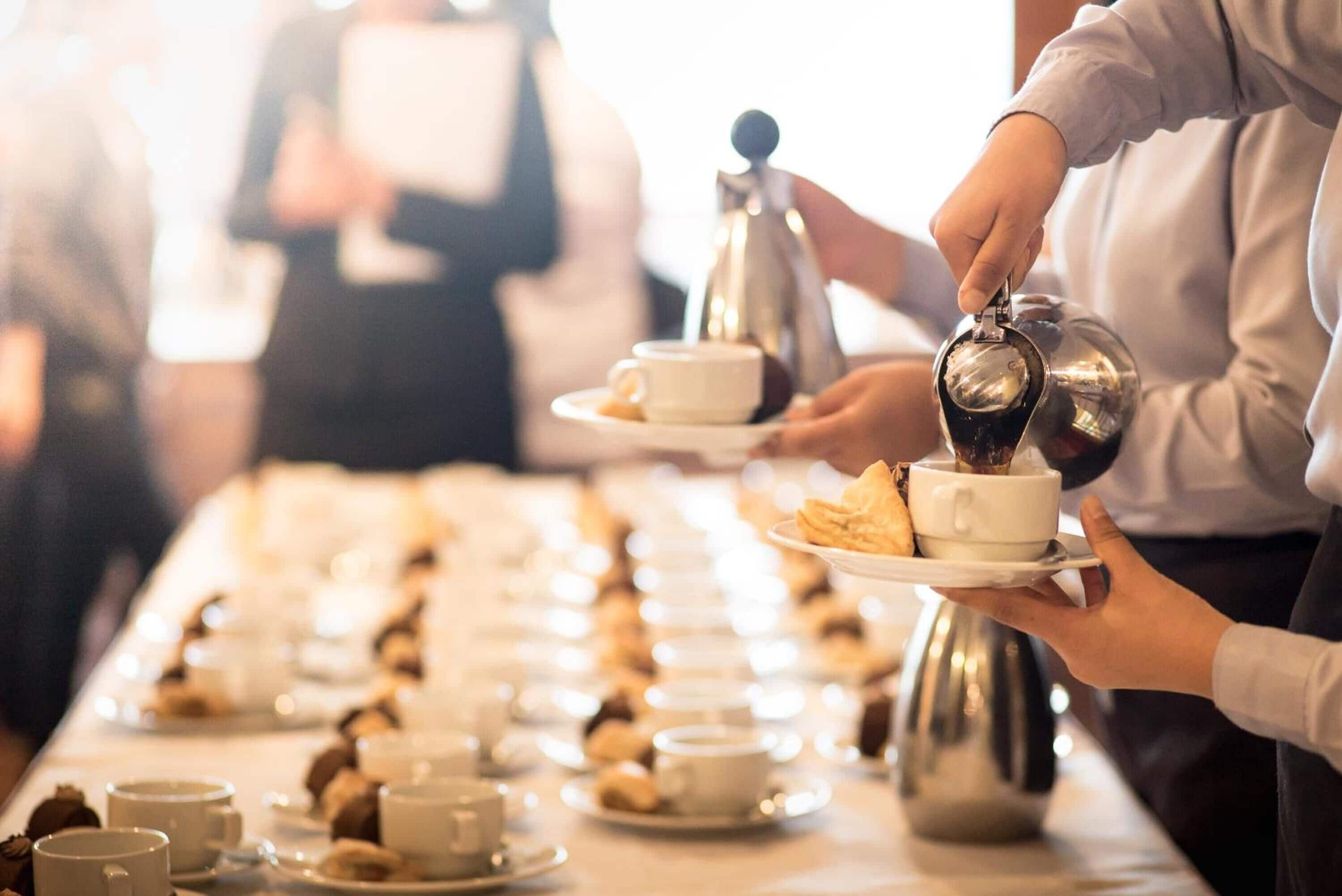 Een buffetopstelling met meerdere aanzitpunten, elk voorzien van een koffiezetapparaat, kopjes en gebak.