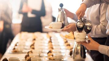 Een buffetopstelling met meerdere aanzitpunten, elk voorzien van een koffiezetapparaat, kopjes en gebak.