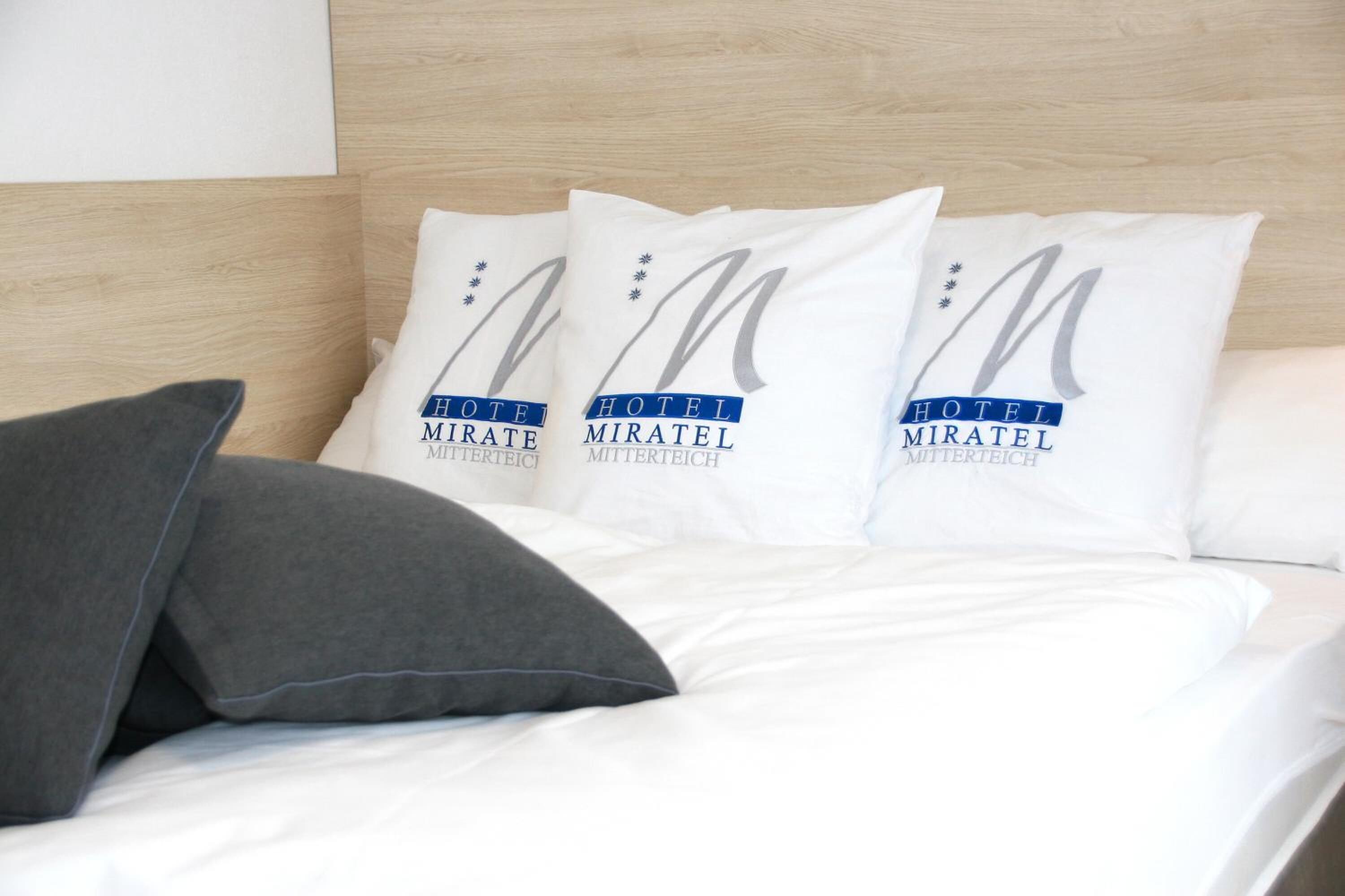 Een hotelbed met witte beddengoed en kussens met het logo van het hotel.