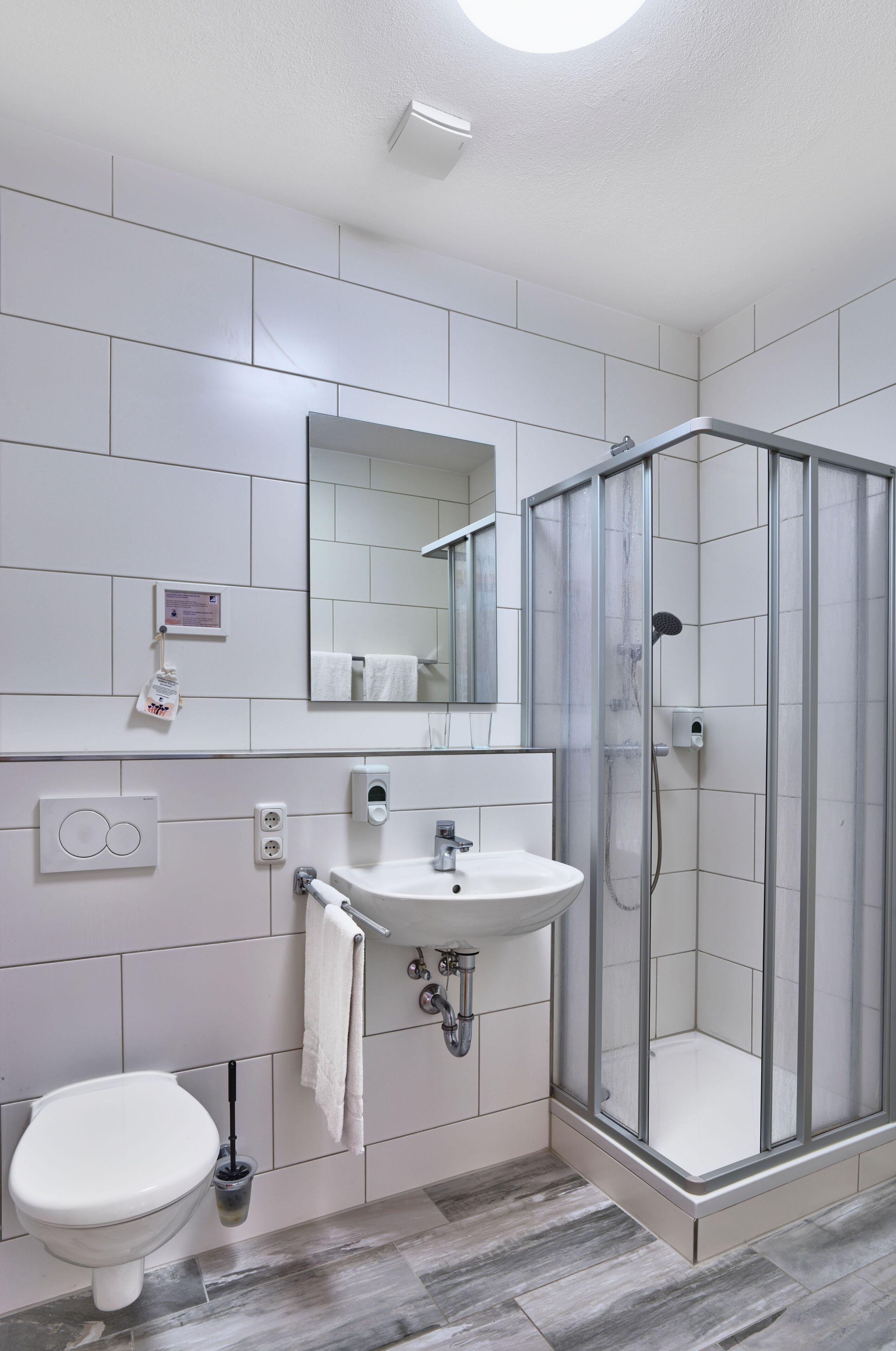 A bathroom with a toilet, sink, mirror, and glass-enclosed shower.