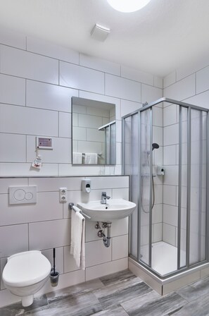Un baño con inodoro, lavamanos, espejo y cabina de ducha de vidrio.