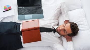 Una persona acostada en una cama con una computadora portátil y un cuaderno a su lado.
