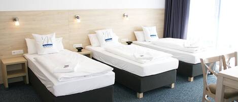 Ein Hotelzimmer mit drei Einzelbetten, jeweils mit Kissen und Nachttisch.
