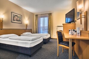 Habitación de hotel con dos camas, un escritorio, un televisor y una ventana con cortinas.