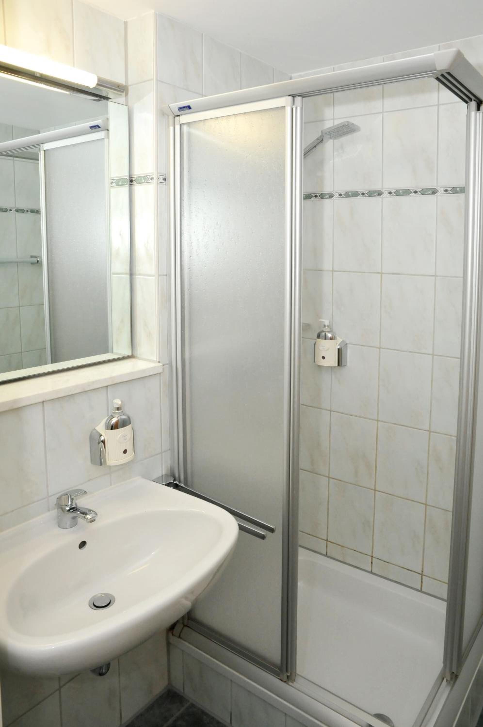Un baño con un lavabo blanco, un espejo y una ducha con mampara de vidrio.