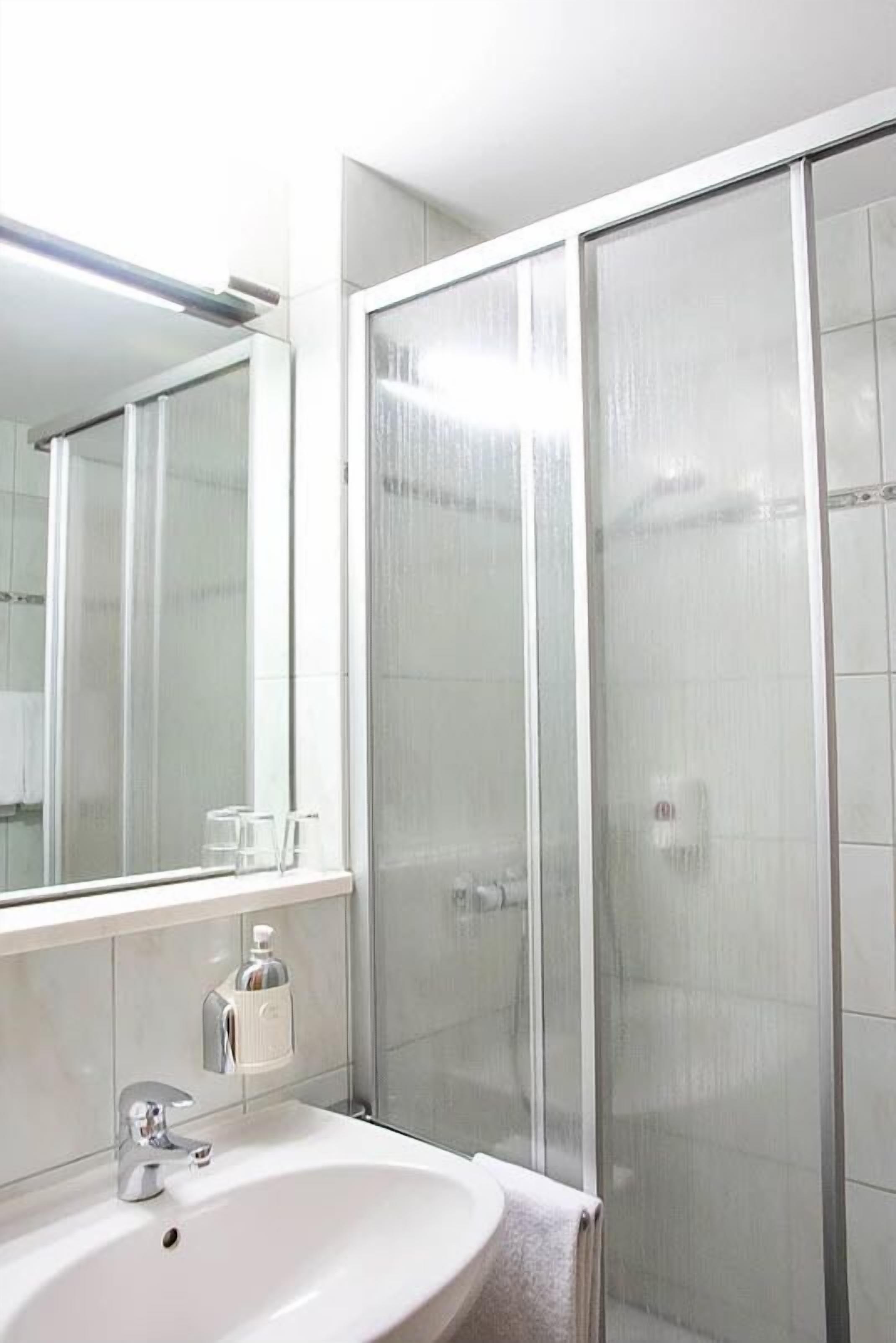 Un baño moderno con un lavamanos blanco, un espejo y una cabina de ducha de vidrio.