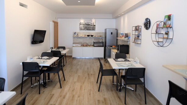 A modern kitchen with a central island, a dining area with four chairs, and a flat-screen TV mounted on the wall. - MozÁrt B&B - Affittacamere (Andria)