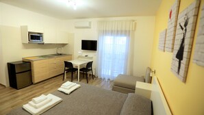 A compact hotel room with a bed, a desk, a kitchenette, and a TV. - MozÁrt B&B - Affittacamere (Andria)