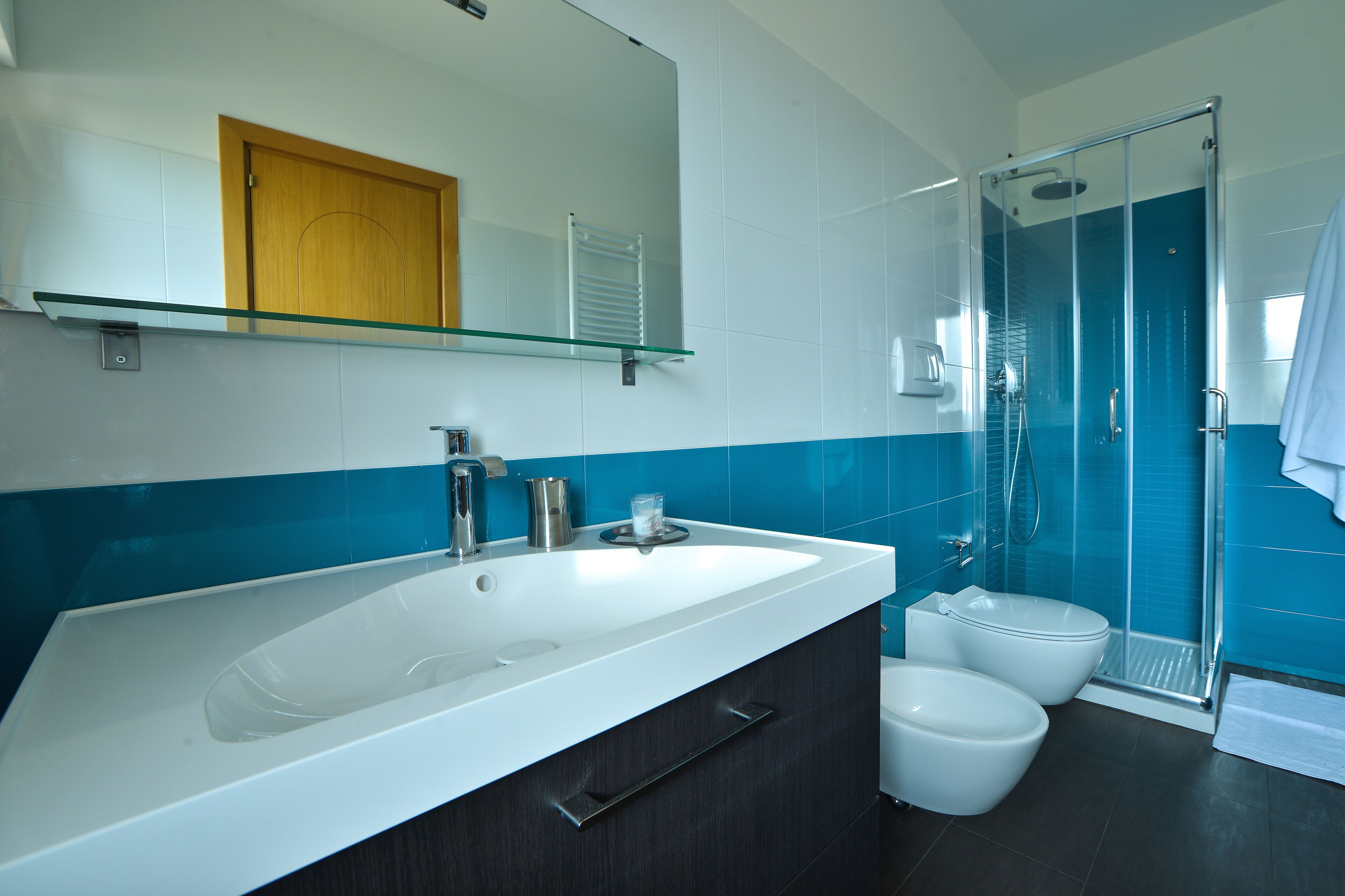 Une salle de bain moderne avec un grand lavabo blanc, une cabine de douche en verre et une porte en bois.