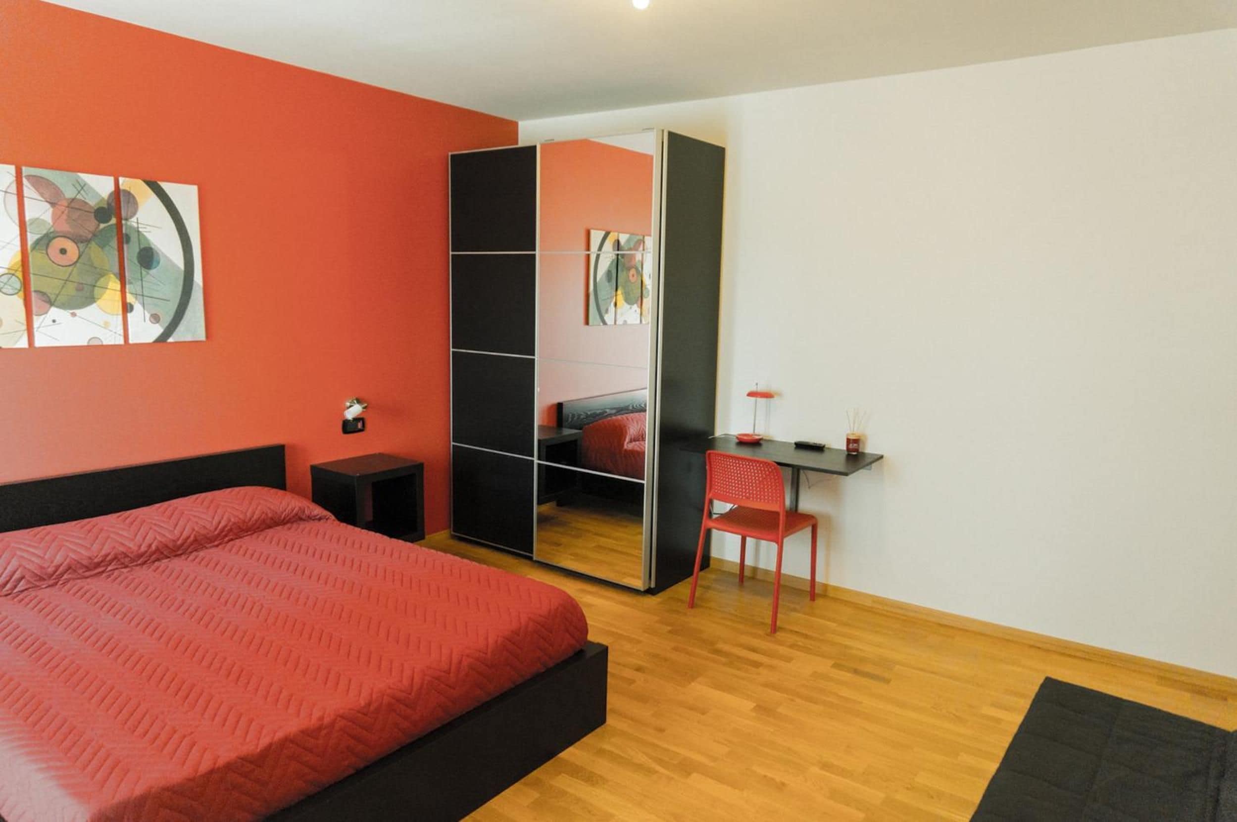 A bedroom with a bed, a desk, a chair, and a mirror.