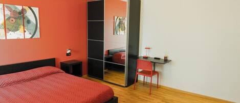 A bedroom with a bed, a desk, a chair, and a mirror.