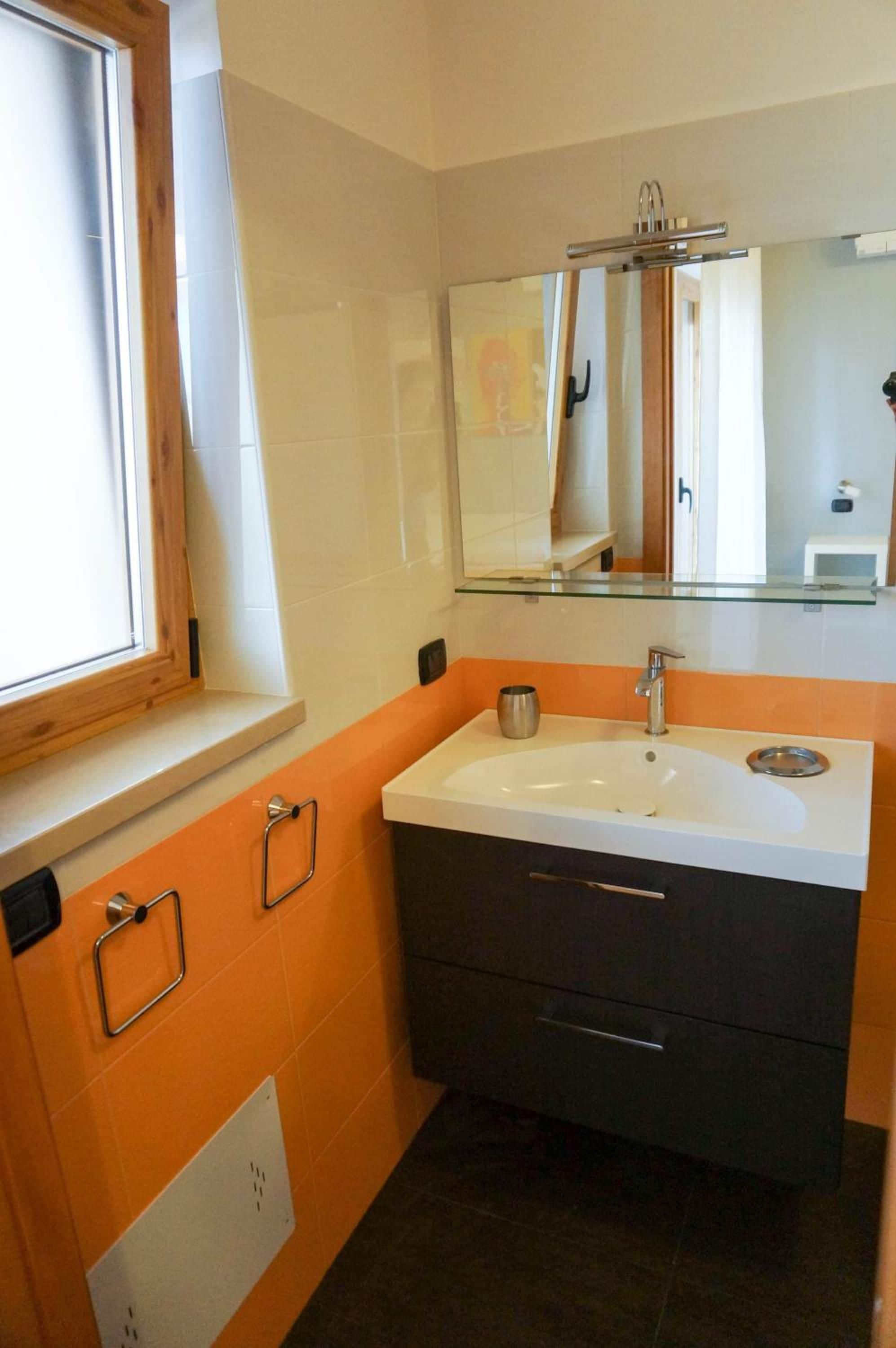 Une salle de bain avec un lavabo blanc, des meubles sombres et une fenêtre avec des cadres en bois.