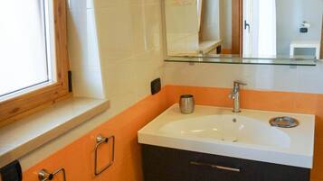 Une salle de bain avec un lavabo blanc, des meubles sombres et une fenêtre avec des cadres en bois.