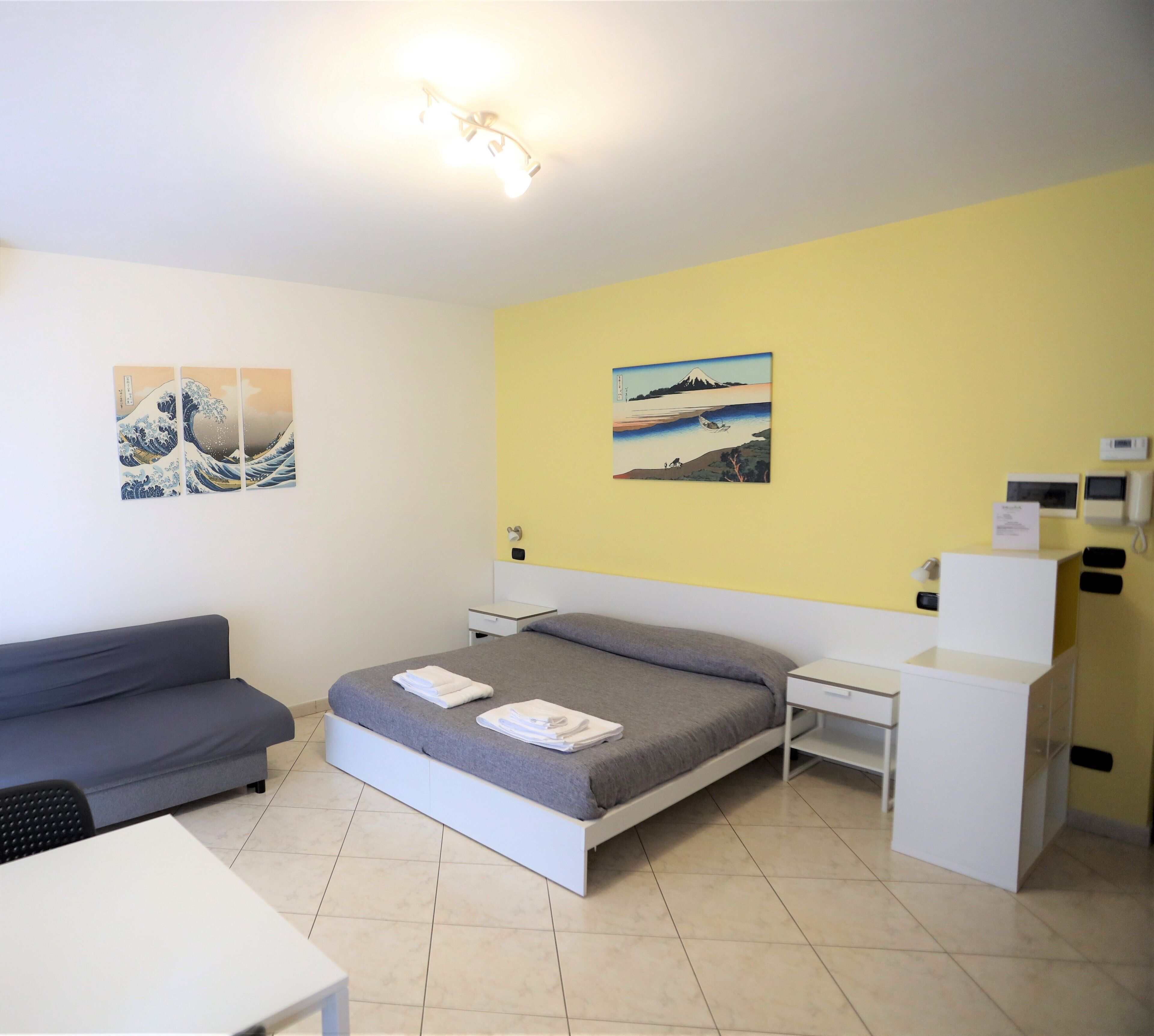 Ein Schlafzimmer mit einem Bett, einem Schreibtisch, einer Couch und zwei Wandbildern.