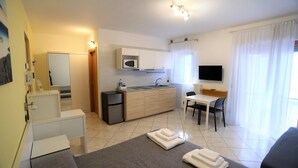 A compact hotel room with a kitchenette, a bed with towels, a desk, and a TV. - MozÁrt B&B - Affittacamere (Andria)