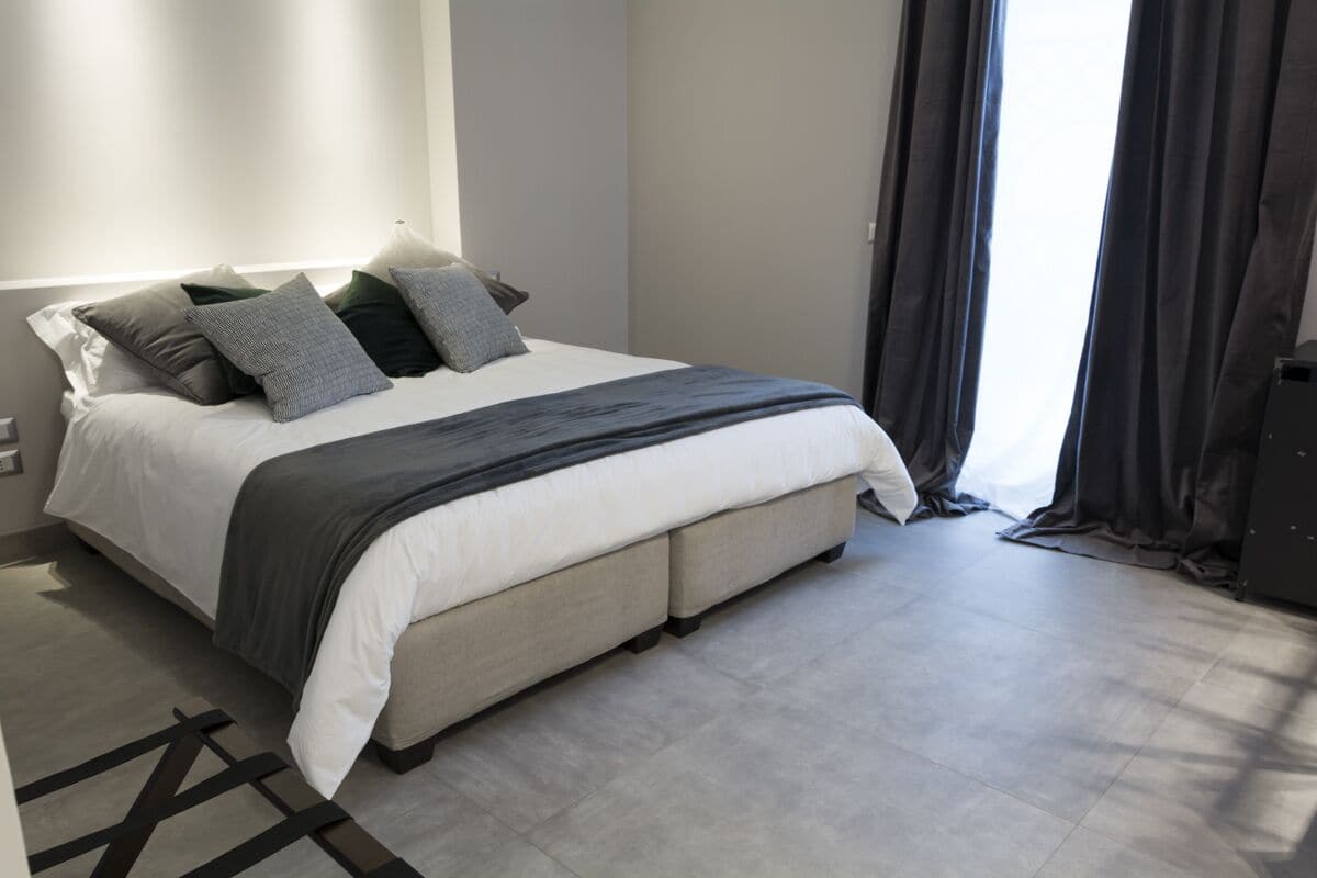 Une chambre à coucher moderne avec un grand lit, une table de chevet, une commode et une fenêtre avec des rideaux.