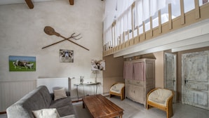 Una sala de estar acogedora con un sofá gris, una mesa de centro de madera, sillas de mimbre, un radiador blanco, una mesita con una lámpara y una puerta de madera.