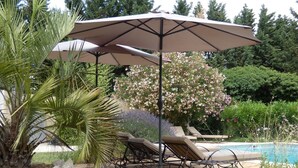 Zona junto a la piscina con sillones de descanso, una terraza de madera y una gran sombrilla que da sombra.