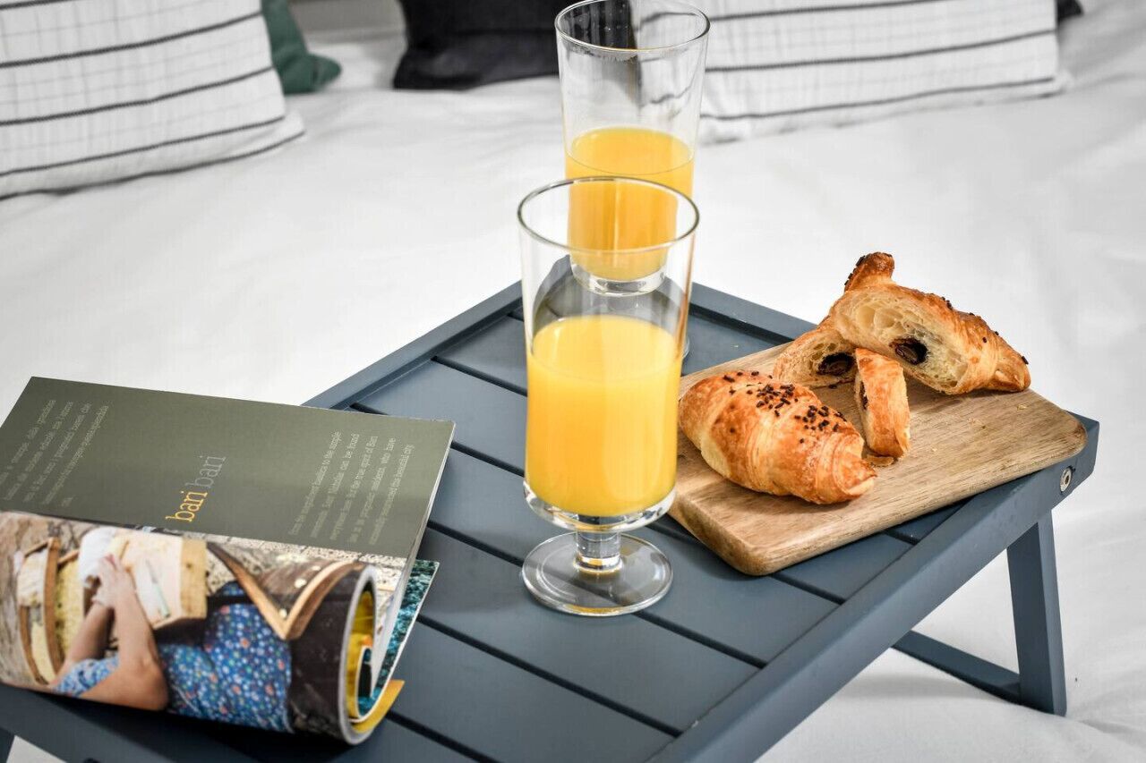 A breakfast tray with croissants and orange juice glasses on a bed with pillows.