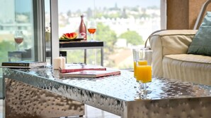 A modern living room with a glass table displaying books, candles, and a glass of orange juice. A sofa with a cushion is visible in the background. - Modern Gem with Stunning Balcony by Sea N Rent (Herzliya)