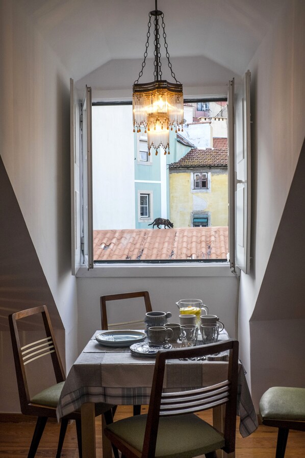 A dining area with a table set for two, a chandelier, and a window with a view of buildings.