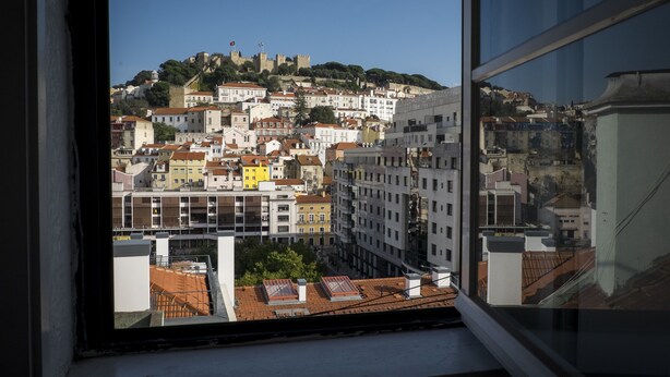 Vista dalla finestra su una città con edifici, una collina con un castello e cielo sereno.