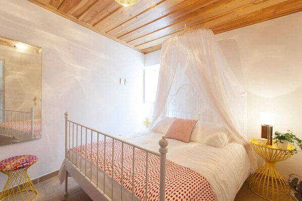 A bedroom with a bed under a canopy, a bedside table with a lamp, a mirror, and a small stool. - Alfama Charming Apartment (Lisbon)