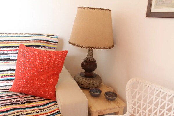 A bed with a colorful striped blanket, a red pillow, a beige lamp, and a small wooden table with two bowls. - Alfama Charming Apartment (Lisbon)