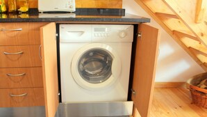 A compact, modern kitchen with wooden cabinetry and a built-in washing machine.