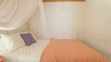 Une chambre à coucher avec un lit, du linge de lit blanc, un oreiller violet, un baldaquin blanc et un plafond en bois.