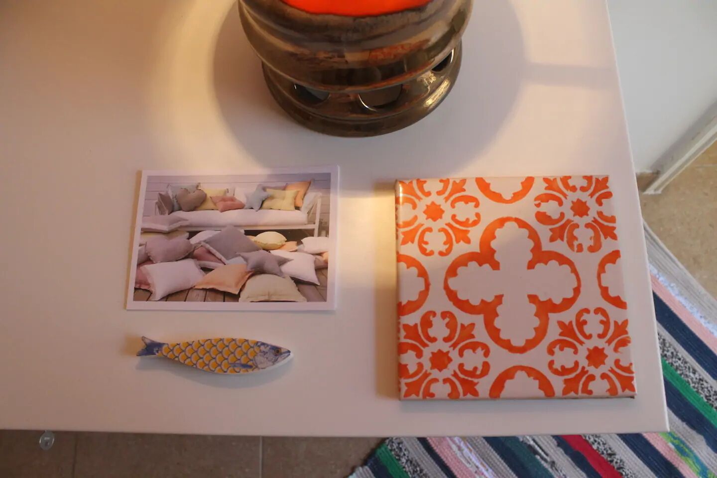 Une table blanche sur laquelle sont posés un cadre contenant une photo d’un canapé et de coussins, un poisson décoratif et une boîte à motifs.