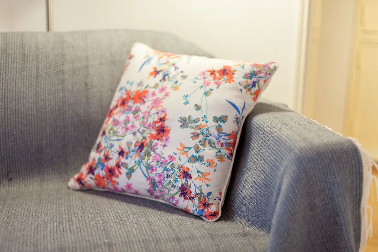 A grey upholstered armchair with a floral pillow.