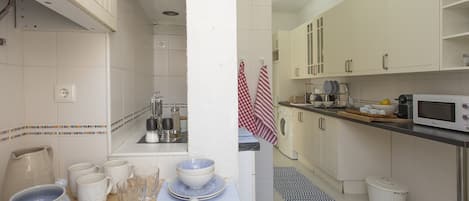 Una cocina con armarios blancos, un microondas, un lavaplatos y diferentes utensilios.