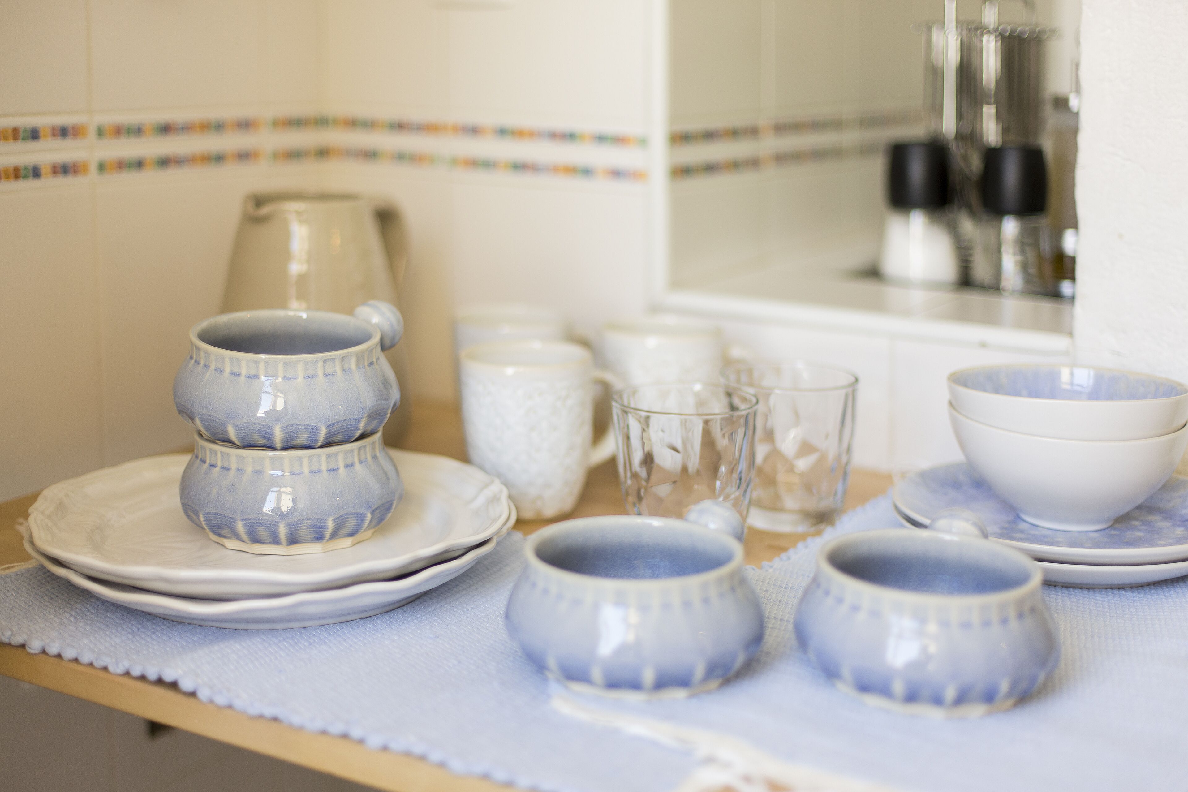 A kitchen counter with stacked plates, bowls, and a kettle.