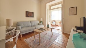 Un salon avec un canapé, une table basse, une lampe, un téléviseur et un tableau accroché au mur.