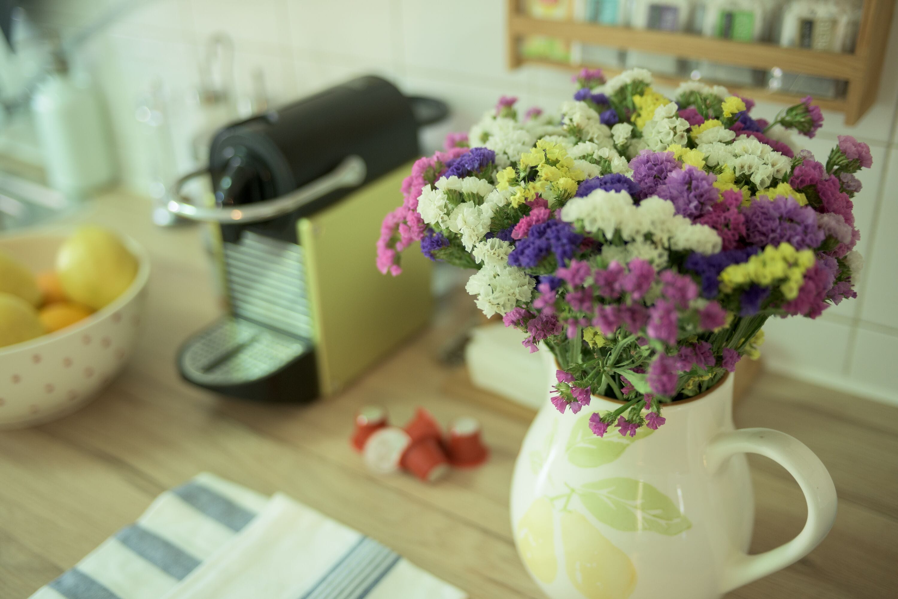 Eine Küchenarbeitsplatte mit einer weißen Vase, gefüllt mit bunten Blumen, einer Reibe und einer Schüssel Zitronen.
