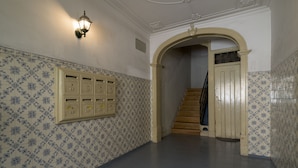 Un pasillo con baldosas estampadas, una lámpara, algunos taquillones y una escalera.