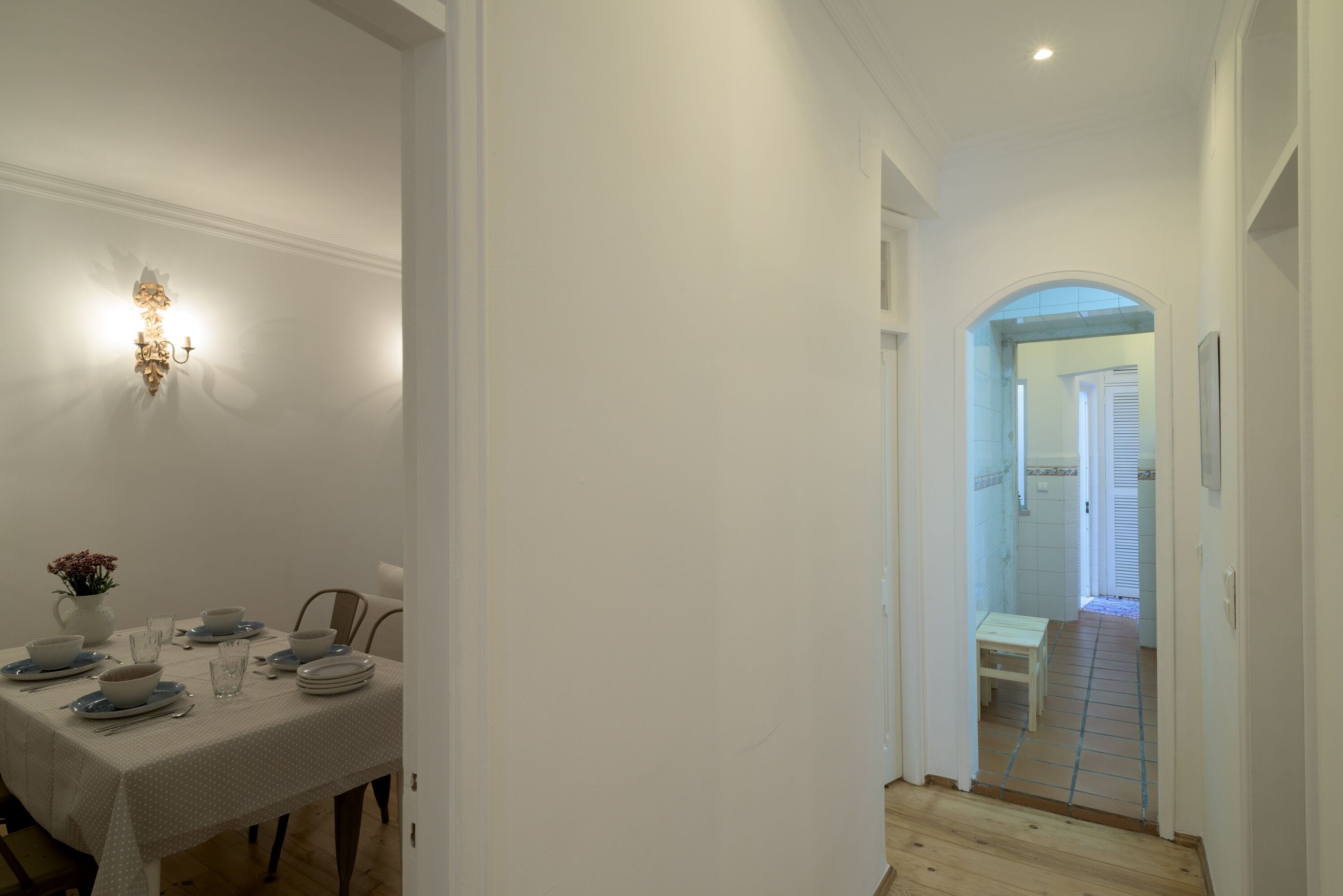 A dining area with a table set for four, a vase with flowers, and a wall-mounted light fixture.