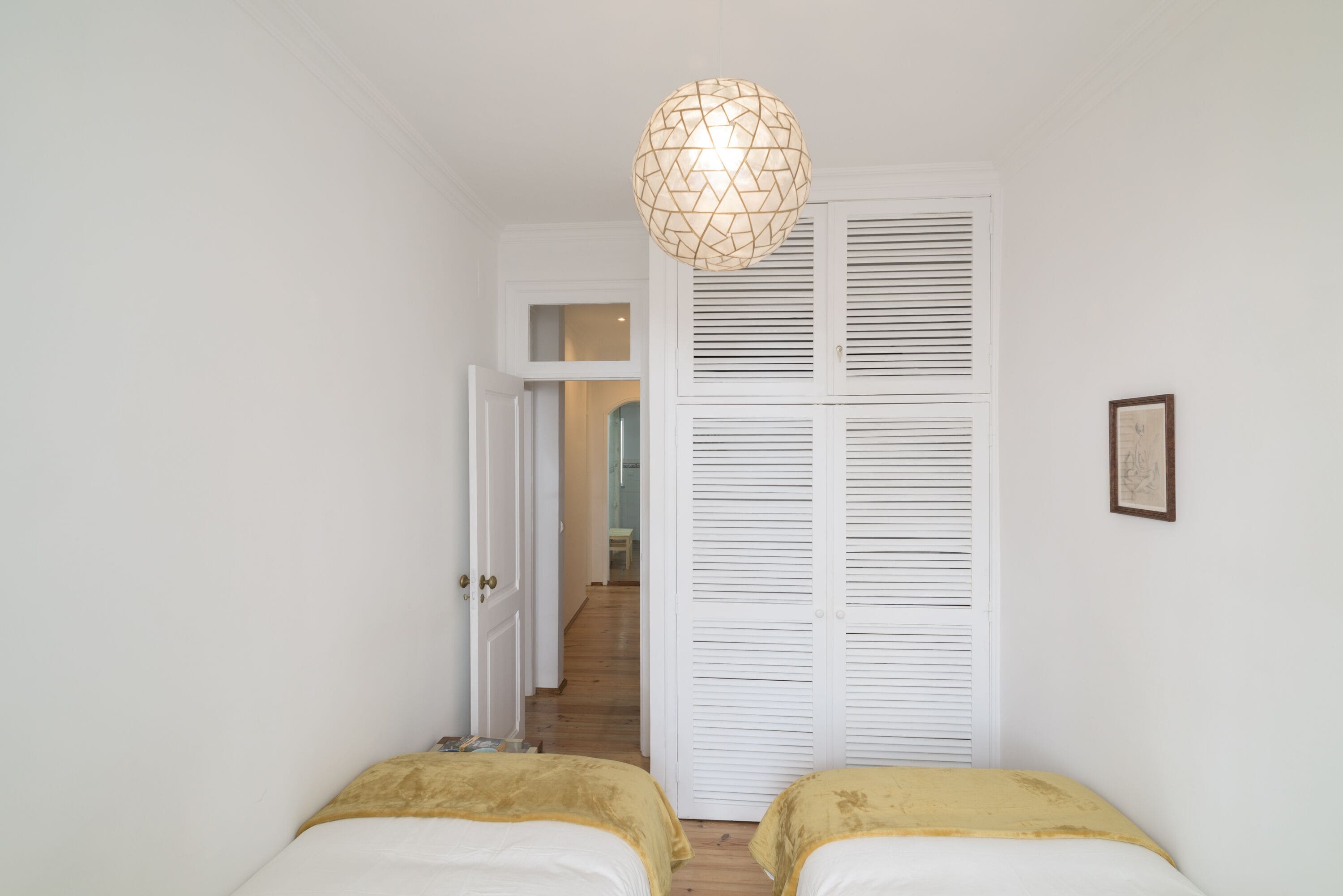 Une chambre avec deux lits, une armoire et un luminaire suspendu.