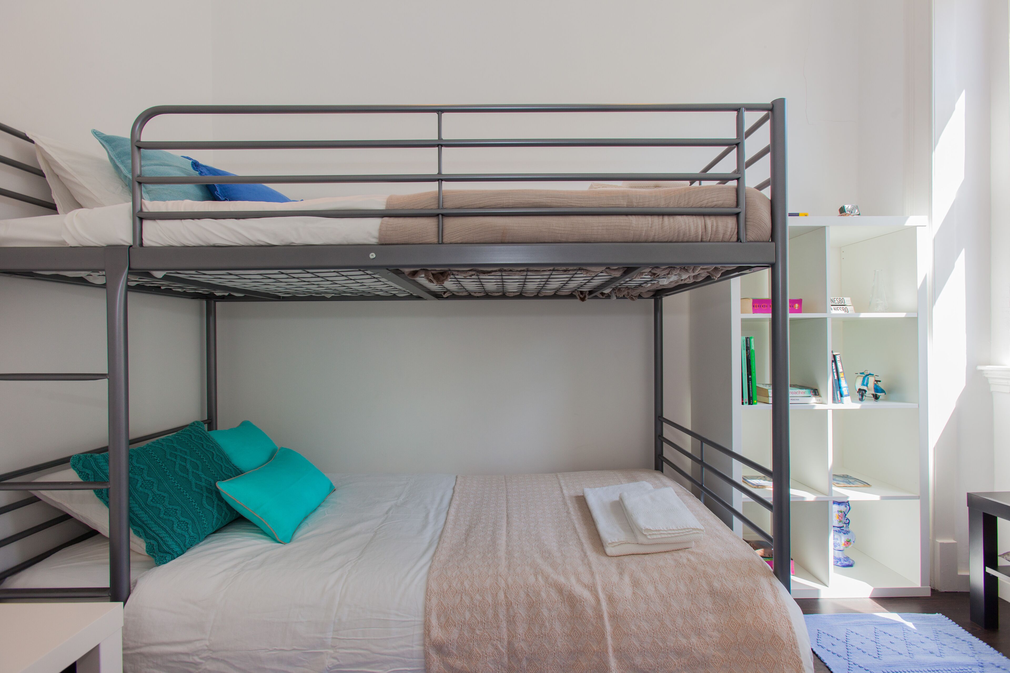 Quarto com beliche, cama de baixo, cama com coberta estampada e estante com livros e objetos decorativos.