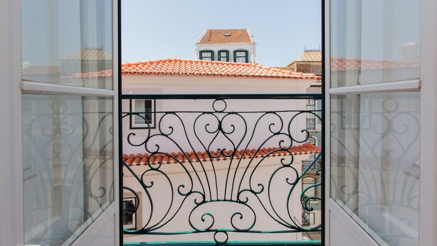 Een balkon met versierde metalen hekwerk en uitzicht op een gebouw met een pannendak.