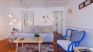 Een gezellige woonkamer met een bank, een blauwe fauteuil, een klein tafeltje met een boek en een kleurrijk vloerkleed.