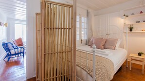 Een slaapkamer met een bed, een wit hoofdeinde, een nachtkastje met een plant en een stoel.
