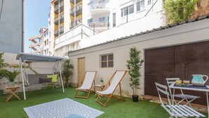A courtyard with artificial grass, two lounge chairs, a small table with a pitcher, and a hanging chair. - Renovated Apartment w/ Private Courtyard, By TimeCooler (Lisbon)