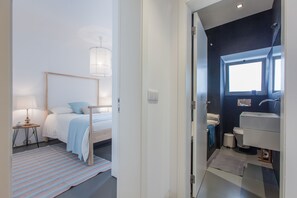 Ein Schlafzimmer mit Bett, Nachttisch, Lampe und Blick ins Badezimmer.