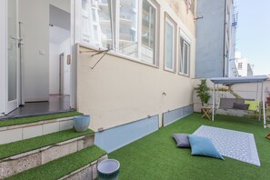 Ein Wohnhaus mit einer kleinen Terrasse, ausgestattet mit Kunstgrasanlage, Sitzgelegenheit inklusive Kissen und einem Blumentopf.