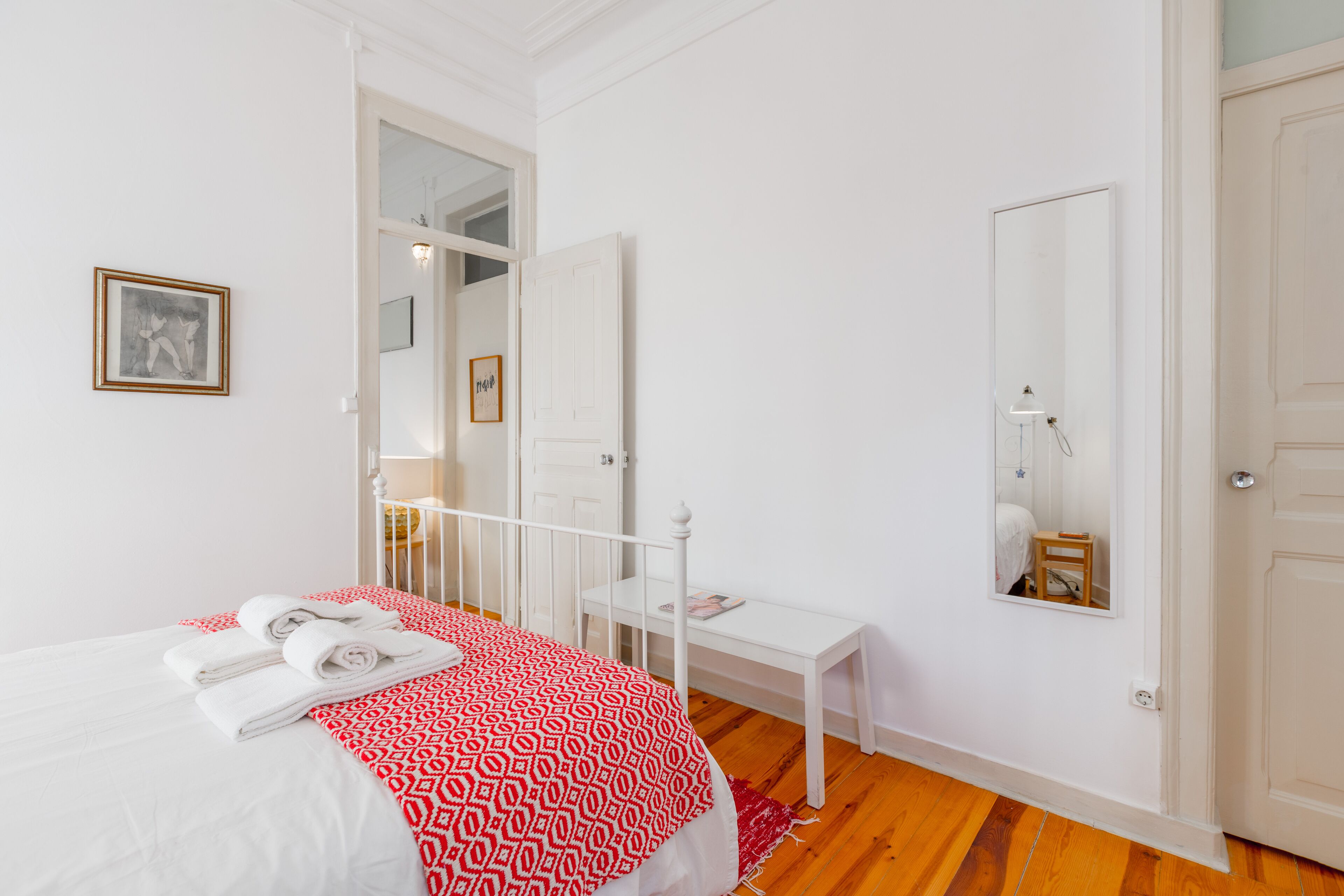 A bedroom with a bed, a bedside table, a mirror, and a door.